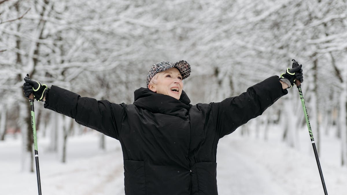 Senior woman celebrates with raised arms while skiing in a snowy park, exuding joy and freedom.